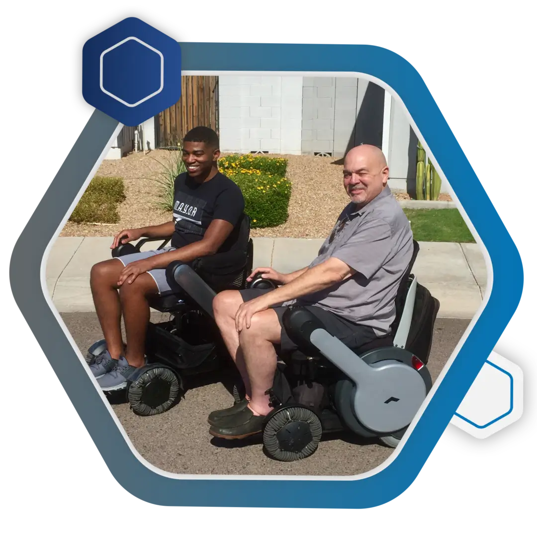 Two men sitting on a wheel chair in front of a hexagon.