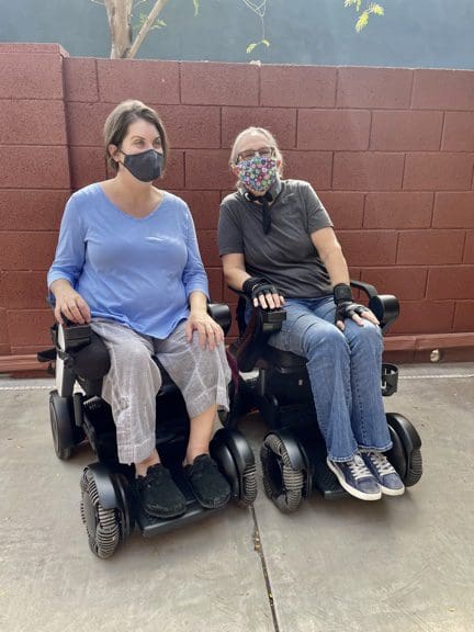 Two people sitting in a wheelchair with masks on.