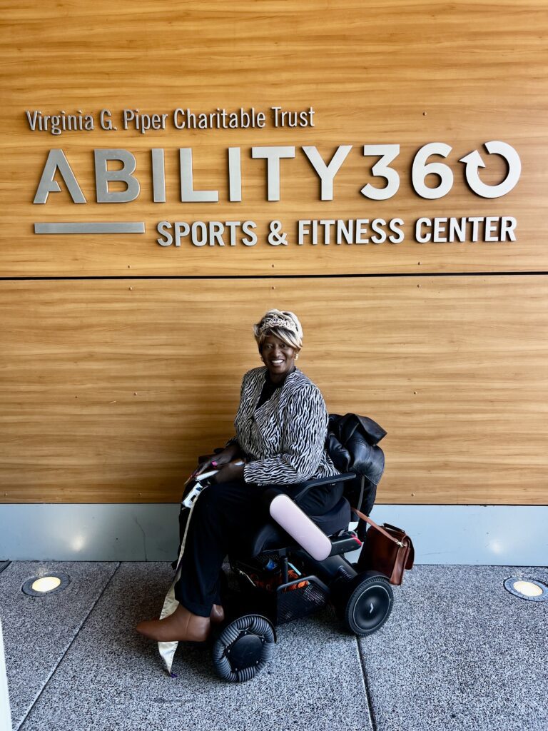 A woman in a wheelchair in front of the ability360 sports and fitness center.