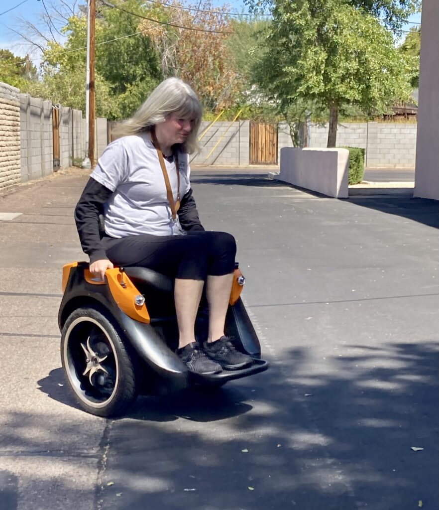 A woman sitting on a wheeled scooter in a parking lot.