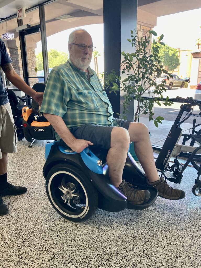 A man is standing next to a blue electric wheelchair.