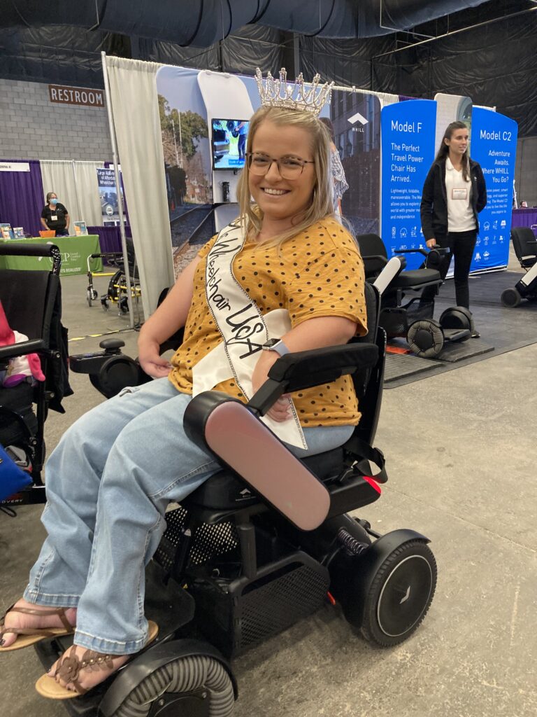 A woman sitting in a wheelchair with a sash.