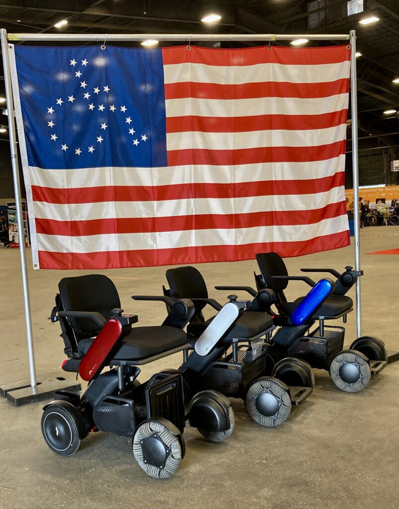 Three wheelchairs with an american flag in front of them.