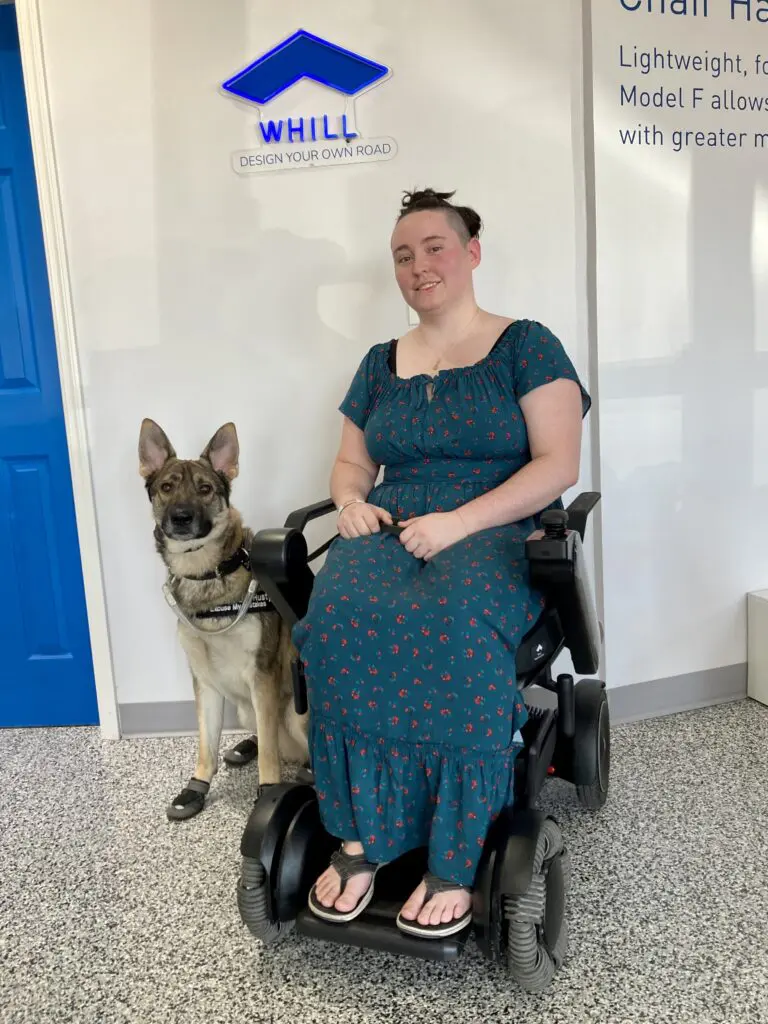 A woman in a wheelchair with a dog in front of a sign.