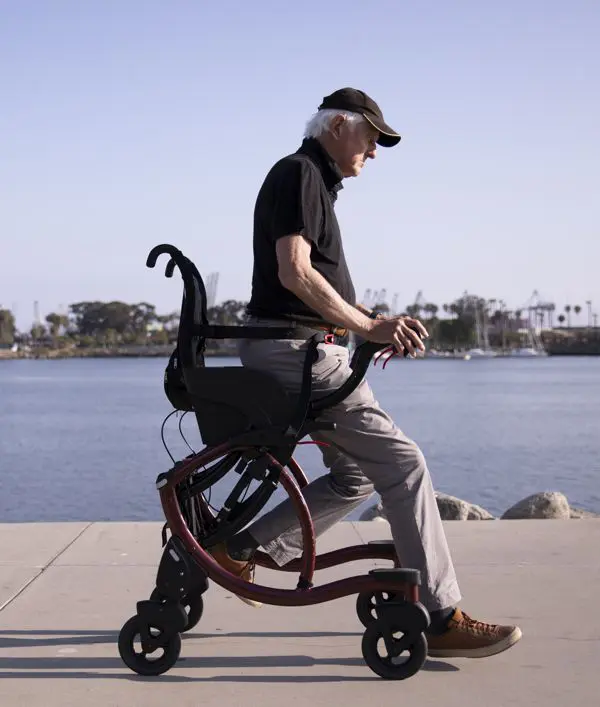 Man walking with a knee walker on a paved path.