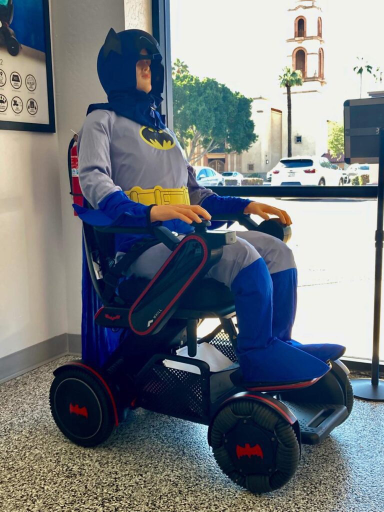 A man dressed as batman sits in a wheelchair.